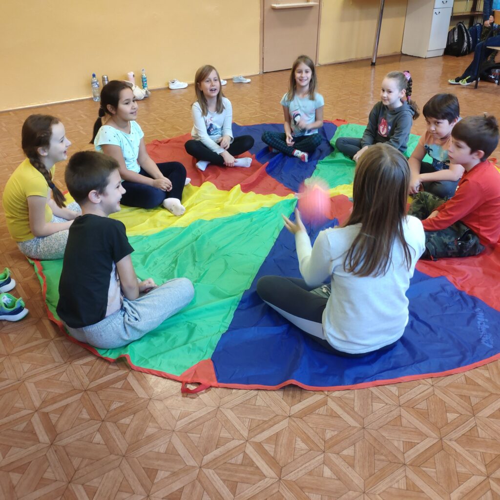 Grupa uczniów siedzi na kolorowej chuście animacyjnej na podłodze