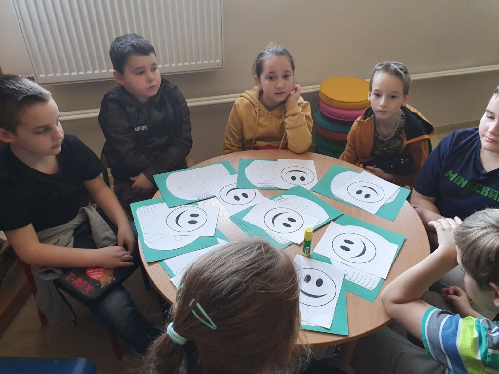 Uczniowie przy stoliku rysują uśmiechnięte buzki