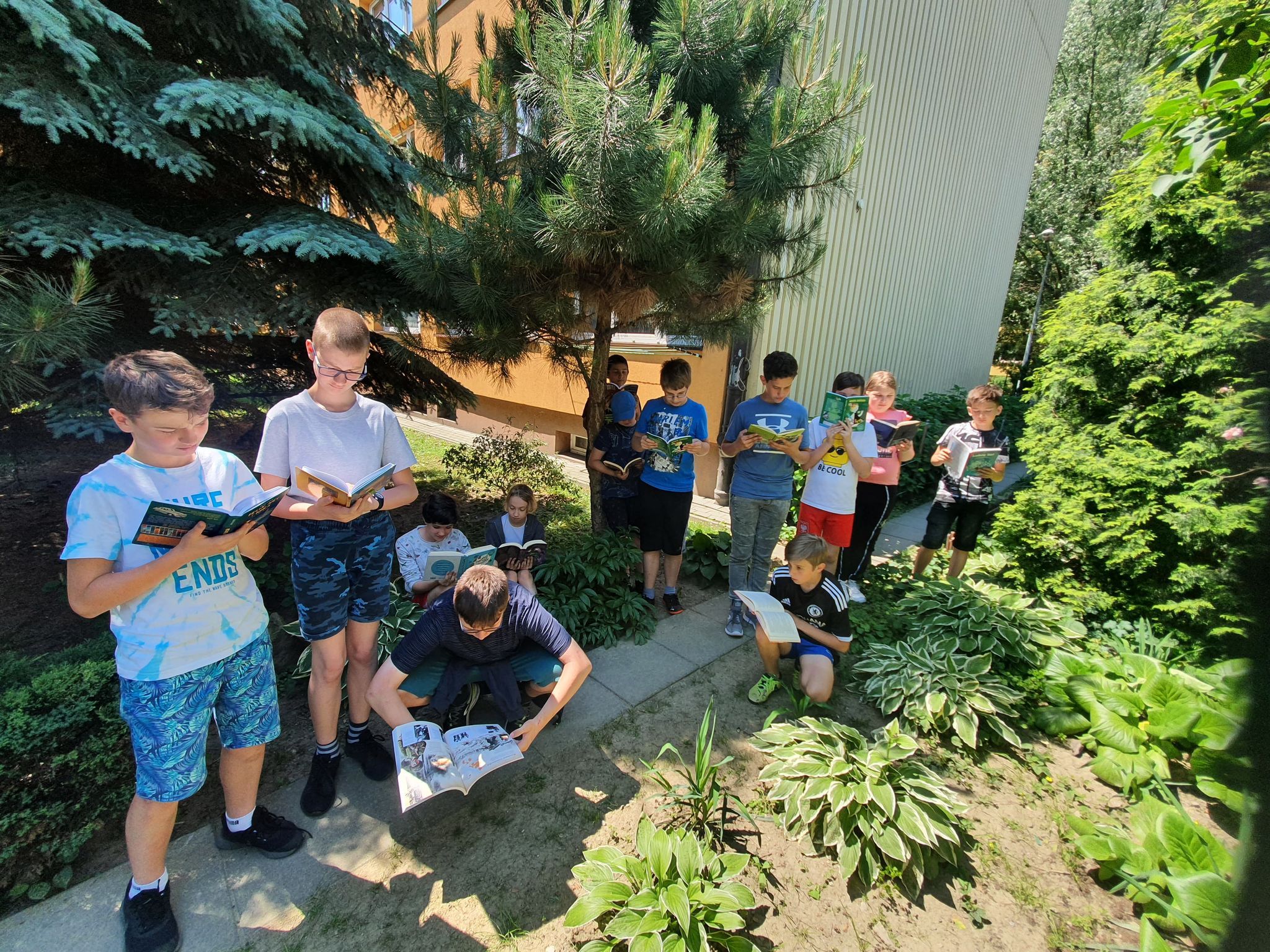 Grupa uczniów czyta książki na terenie wokół szkoły.